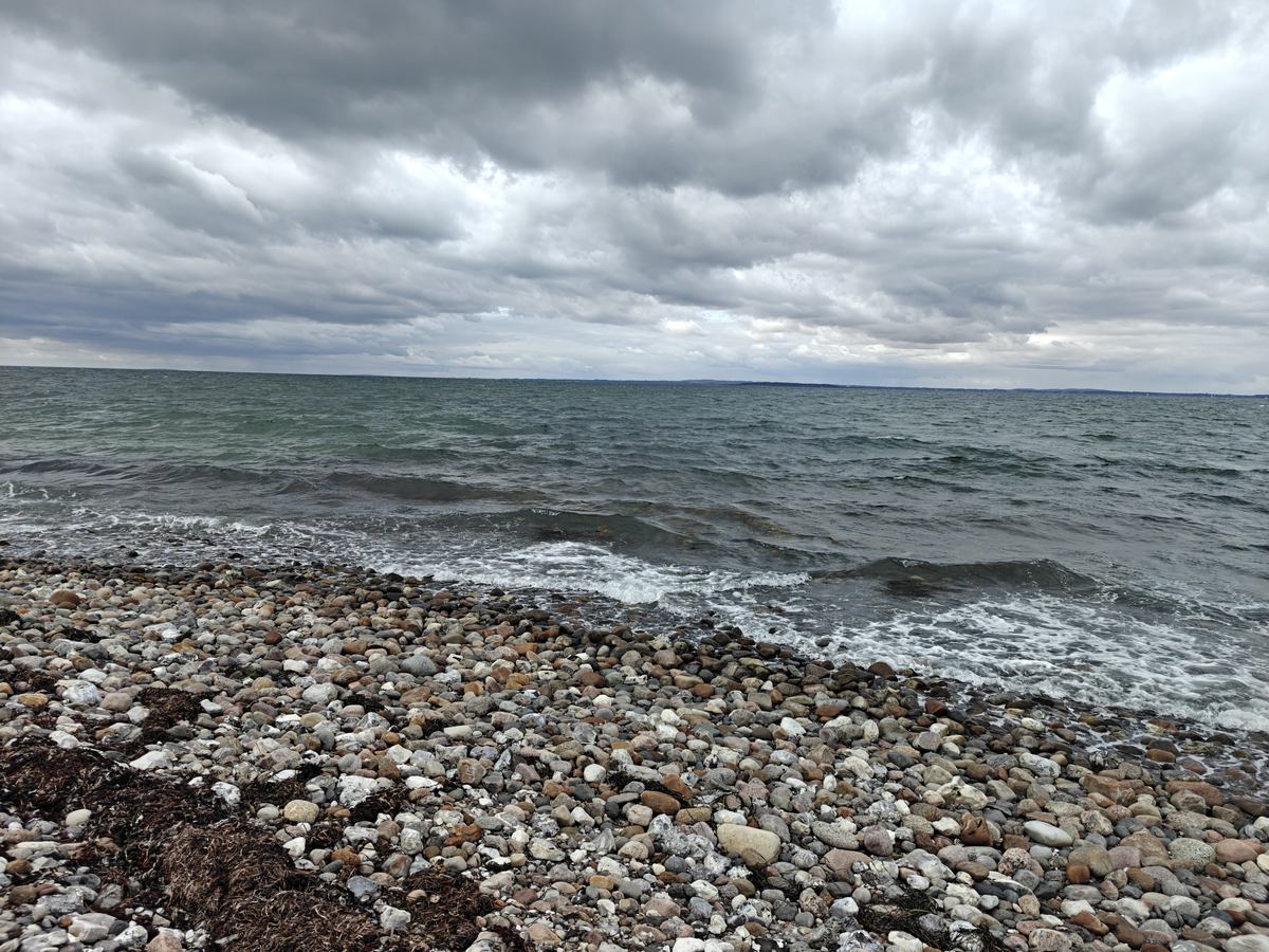Stenet strand under en grå, skyet himmel, med bølger der skyller ind