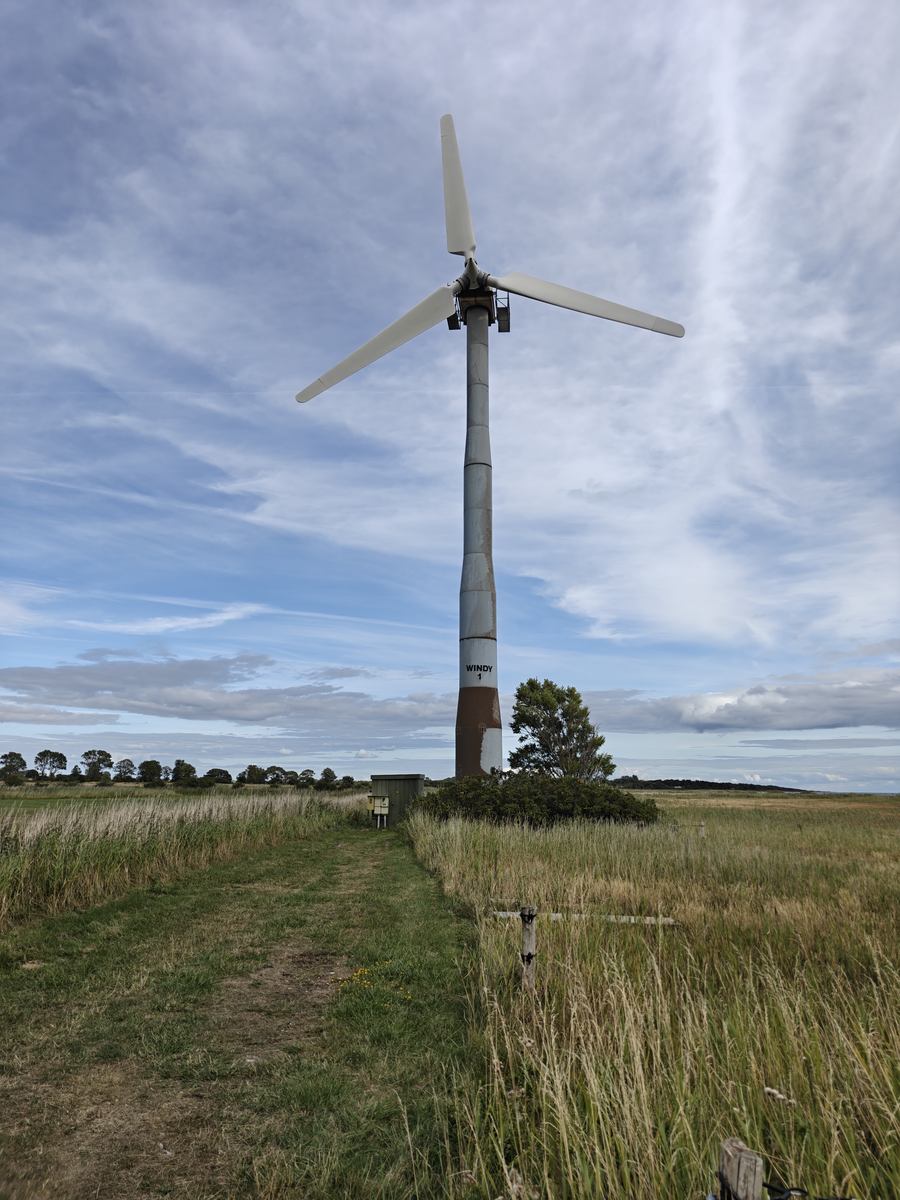 Gammel vindmølle med tre vinger, mærket WINDY 1, set nedefra mod en delvist skyet himmel