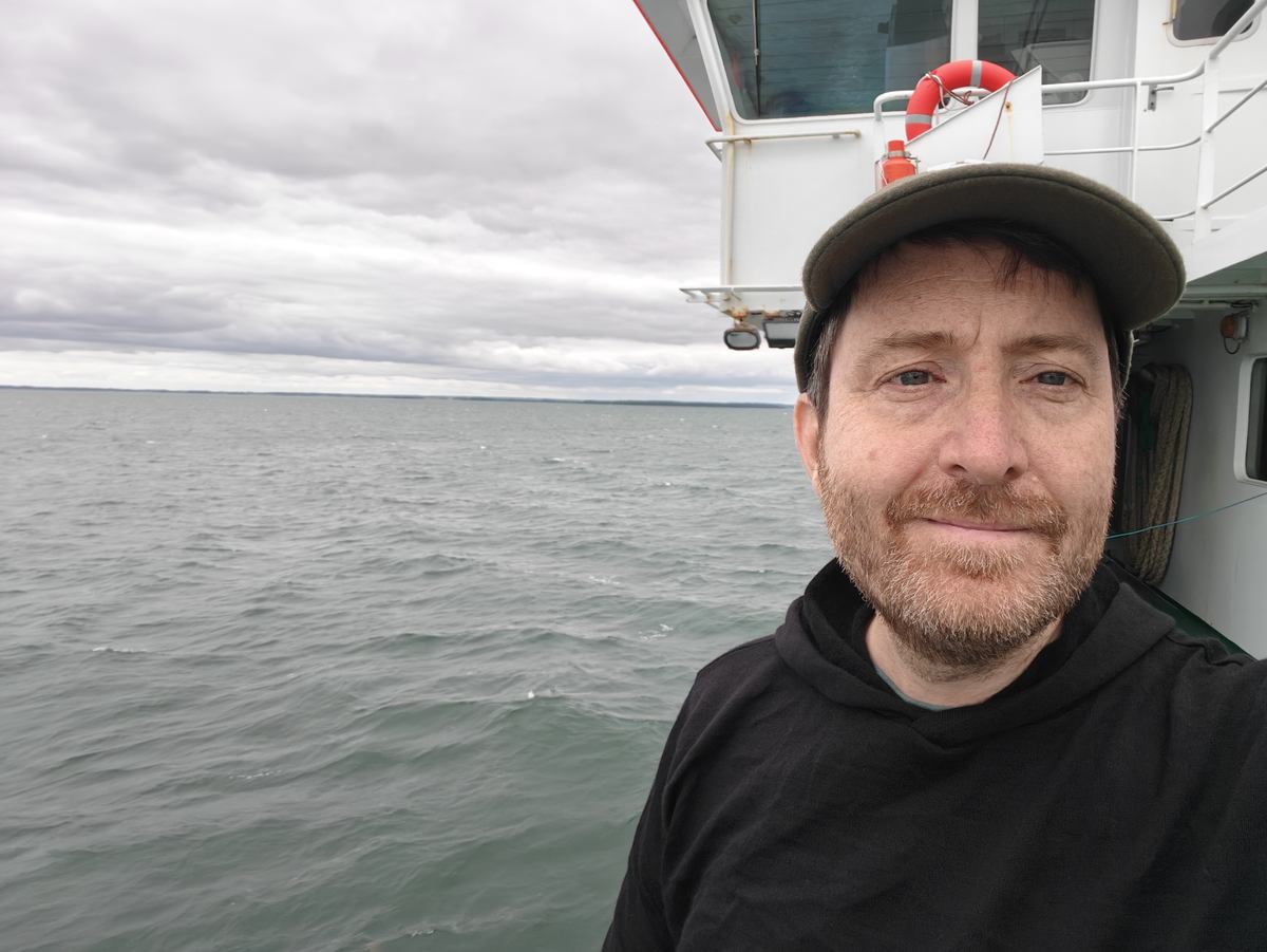 Selfie ombord på hjemfærgen, i gul jakke, med redningskrans og styrehus i baggrunden