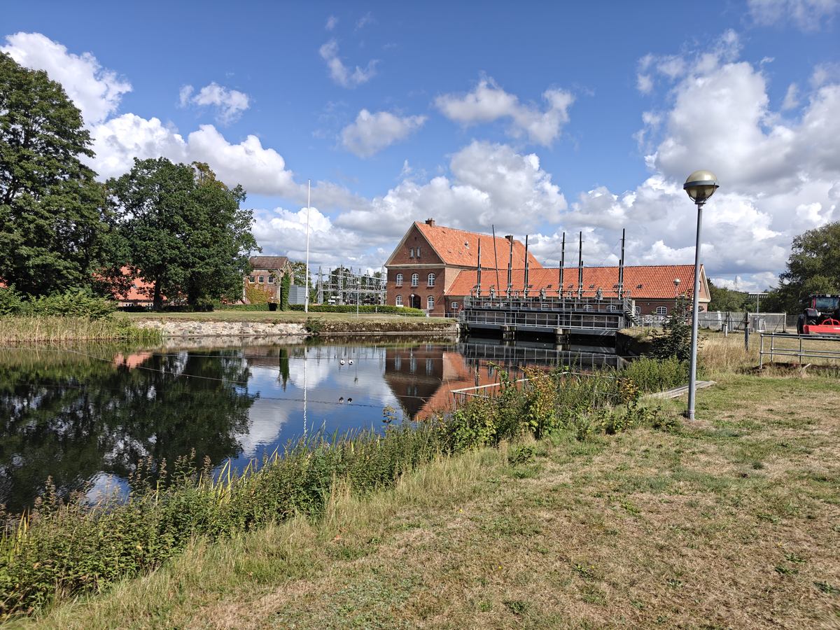 Kanal med rødt bindingsværkshus og en gangbro, spejlet i det stille vand